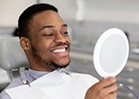 Man smiling while looking at reflection in handheld mirror