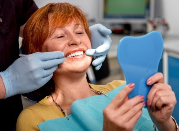 Woman looking at her beautiful smile after dental crown and bridge restoration