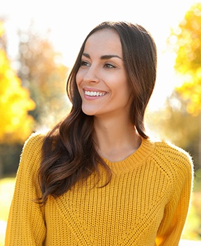 A young woman wearing a yellow sweater and smiling after seeing a dentist in Phoenix about a dental crown