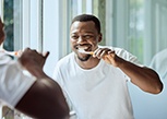 Man smiling while brushing his teeth in bathroom