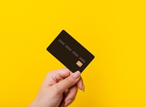 Manicured hand holding payment card against yellow background
