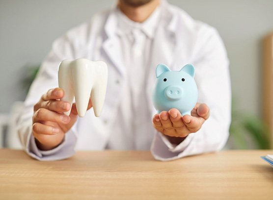 Dentist holding model tooth and blue piggy bank