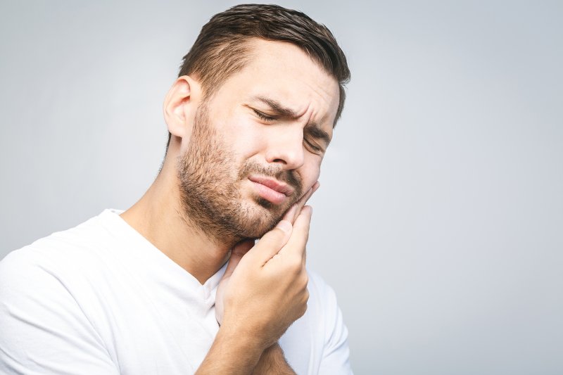 person with toothache who needs emergency dental visit holding cheek